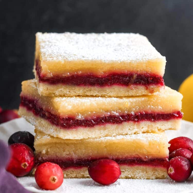 three layered lemon cranberry bars, stacked on a small white plate, garnished with fresh cranberries.