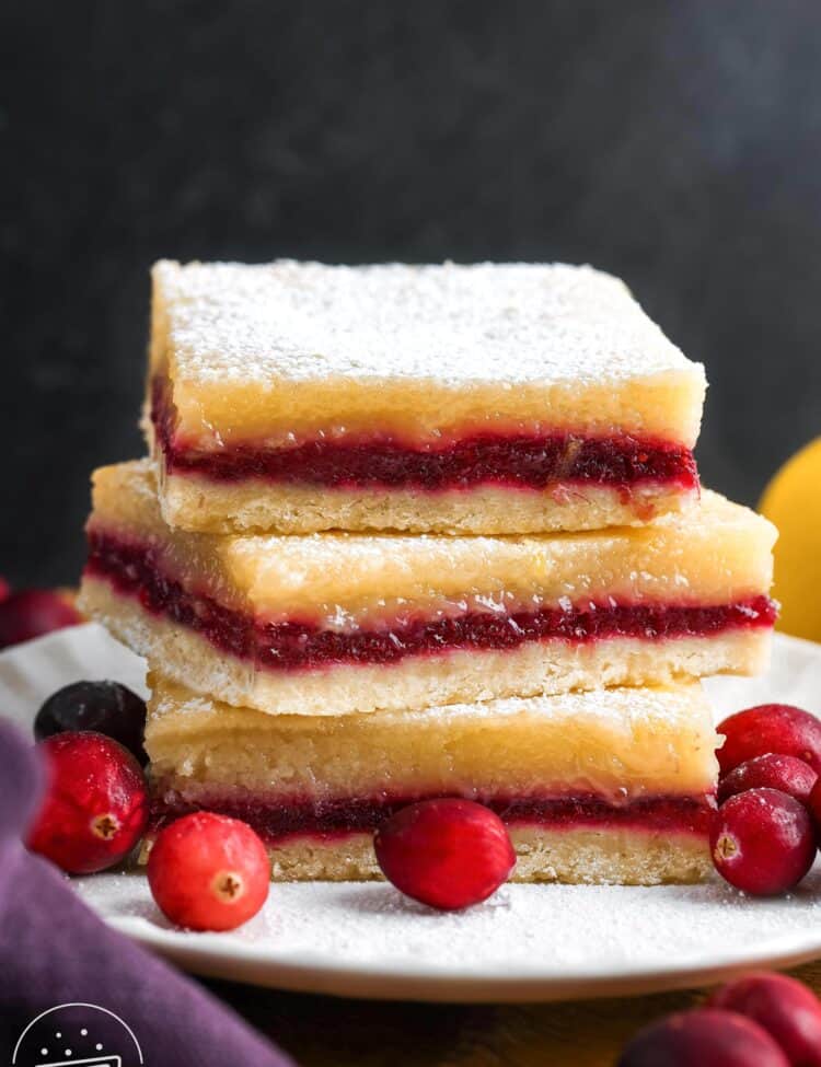 three layered lemon cranberry bars, stacked on a small white plate, garnished with fresh cranberries.