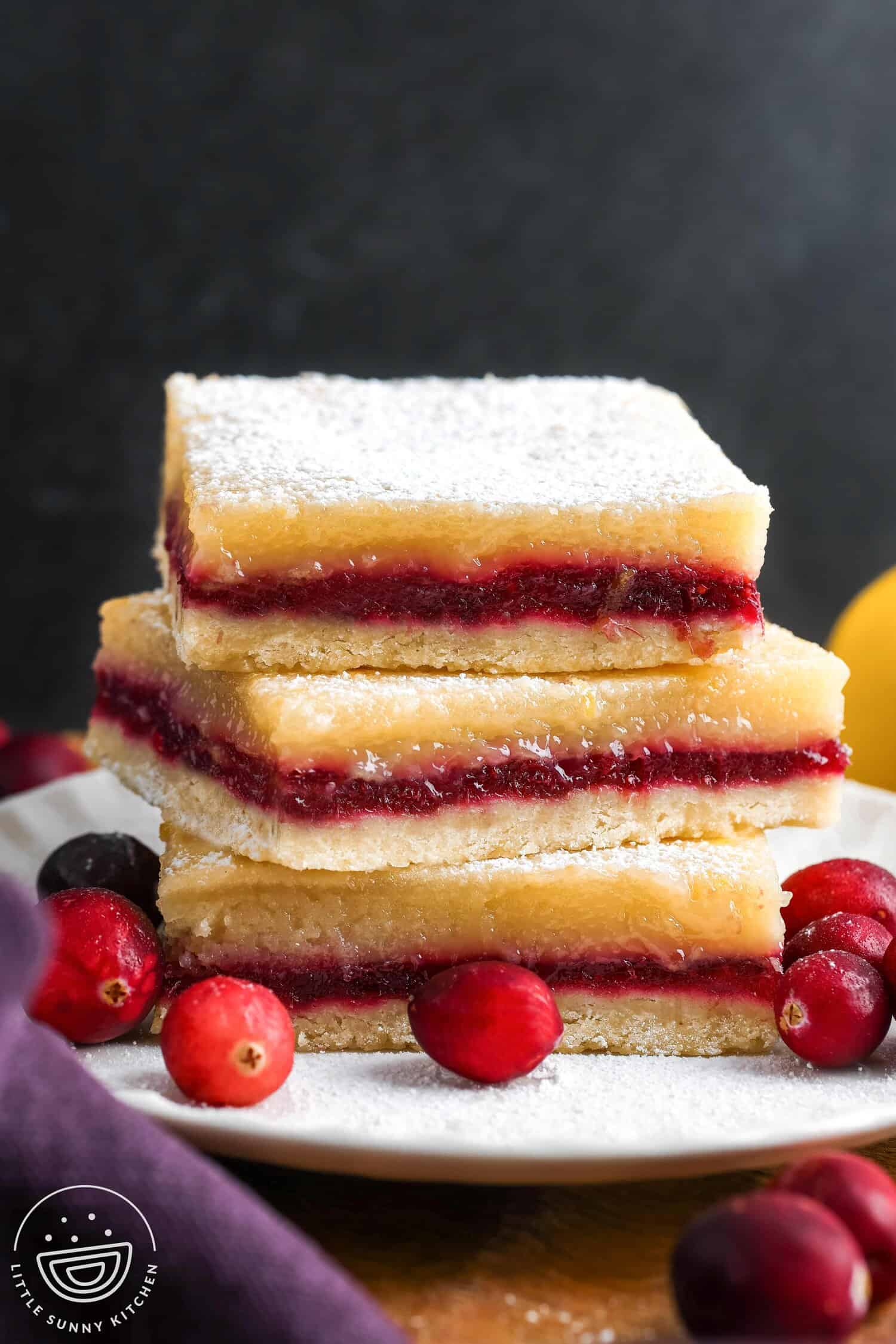 three layered lemon cranberry bars, stacked on a small white plate, garnished with fresh cranberries.