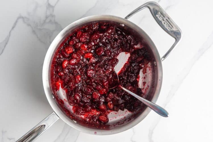 fresh cranberries cooked with sugar in a medium saucepan that is set on a marble counter.