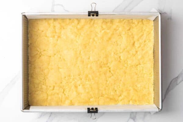 lemon cranberry bar crust pressed into a metal baking pan that is lined with parchment paper.