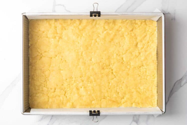 lemon cranberry bar crust pressed into a metal baking pan that is lined with parchment paper.