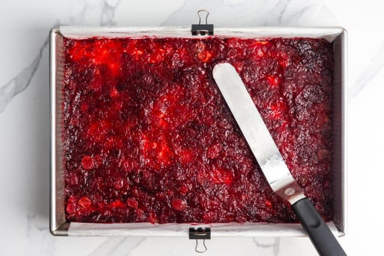 an offset spatula spreading cranberry sauce over a crust to make it smooth and even.