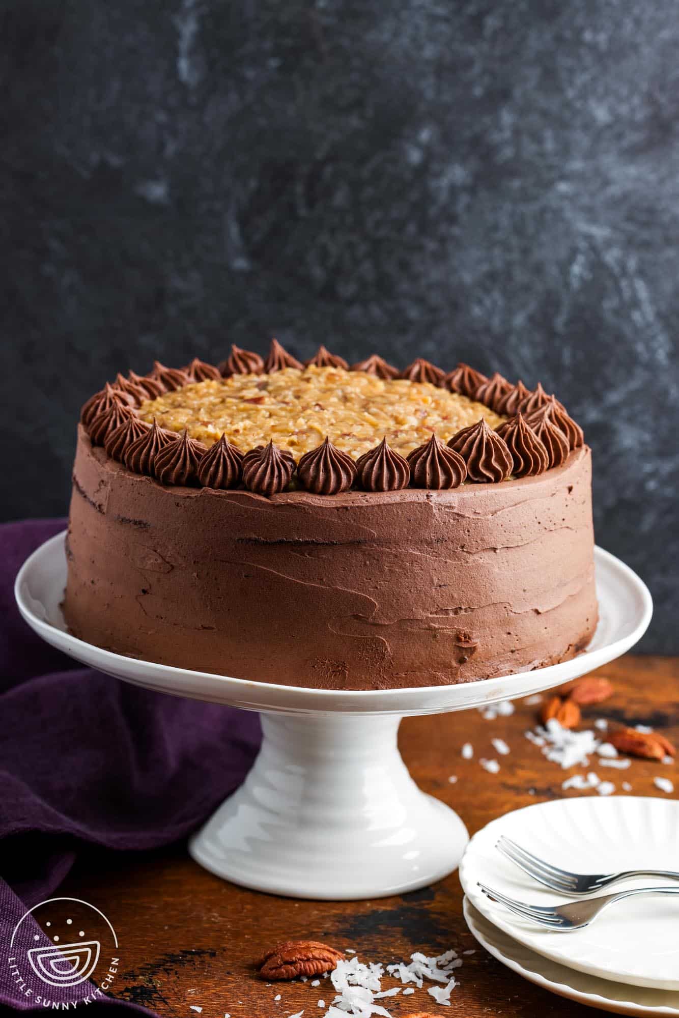 a whole three layer german chocolate cake on a white pedestal.