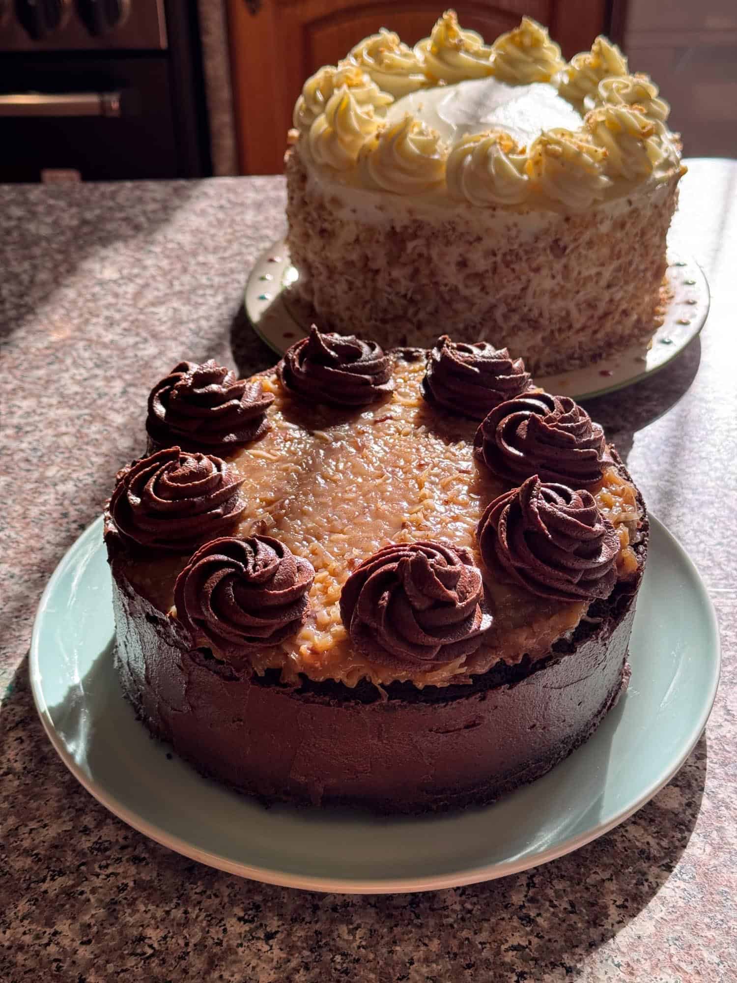 A homemade german chocolate cake on a sunlit counter, in front of another layer cake.
