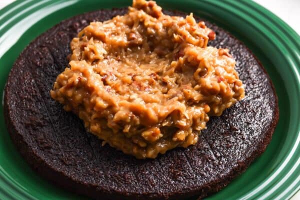 coconut filling added to one layer of german chocolate cake that is set on a dark green platter.