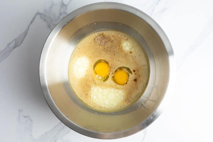 eggs, milk, and vegetable oil added to a large metal mixing bowl, set on a marble counter.