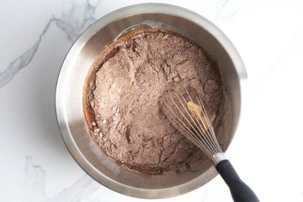 dry ingredients added to wet ingredients to make a german chocolate cake batter in a metal bowl with a whisk.