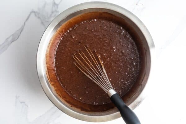 deep brown German chocolate cake batter whisked in a metal mixing bowl that is set on a white marble counter.