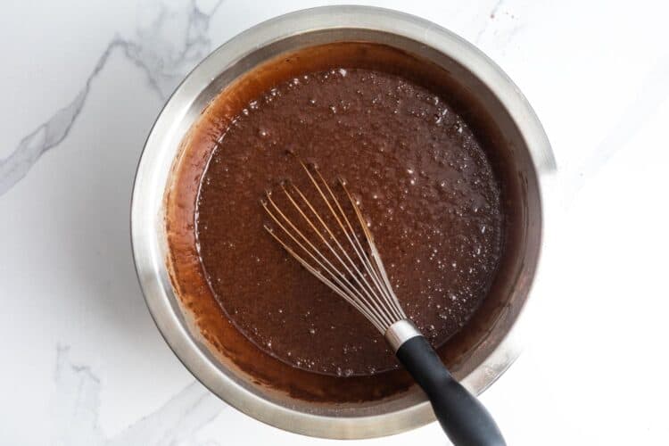 deep brown German chocolate cake batter whisked in a metal mixing bowl that is set on a white marble counter.