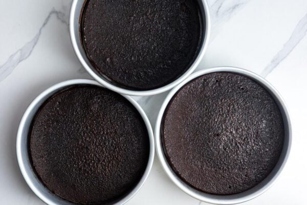 three baked german chocolate layer cakes, cooling in their round pans.