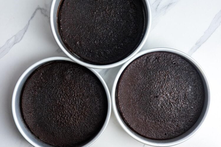 three baked german chocolate layer cakes, cooling in their round pans.