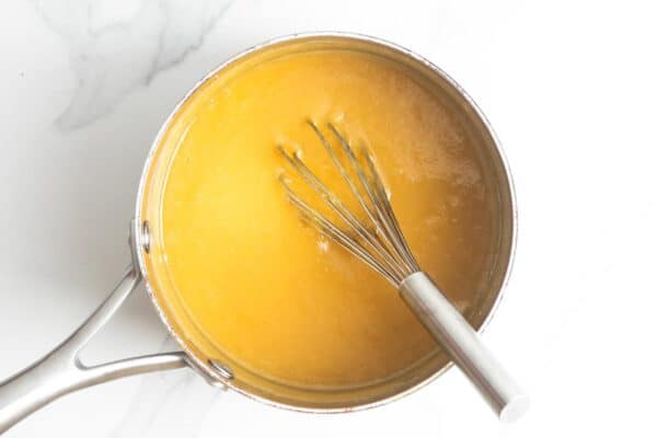 evaporated milk, egg yolks, brown sugar, and butter cooking in a saucepan, stirred with a wire whisk.