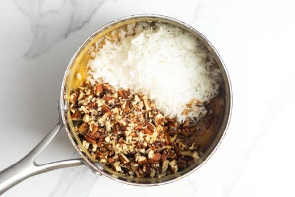shredded coconut and chopped pecans added to caramel to create the filling for german chocolate cake.