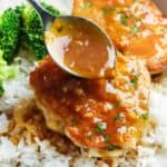 Orange glazed chicken thighs over rice. A spoon is adding extra orange garlic sauce on top of the chicken.