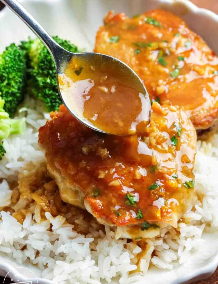 Orange glazed chicken thighs over rice. A spoon is adding extra orange garlic sauce on top of the chicken.