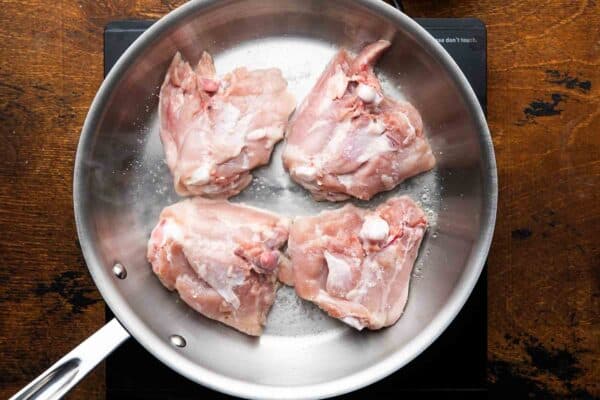 chicken thighs added to a cold stainless steel skillet, skin side down to render the skin.