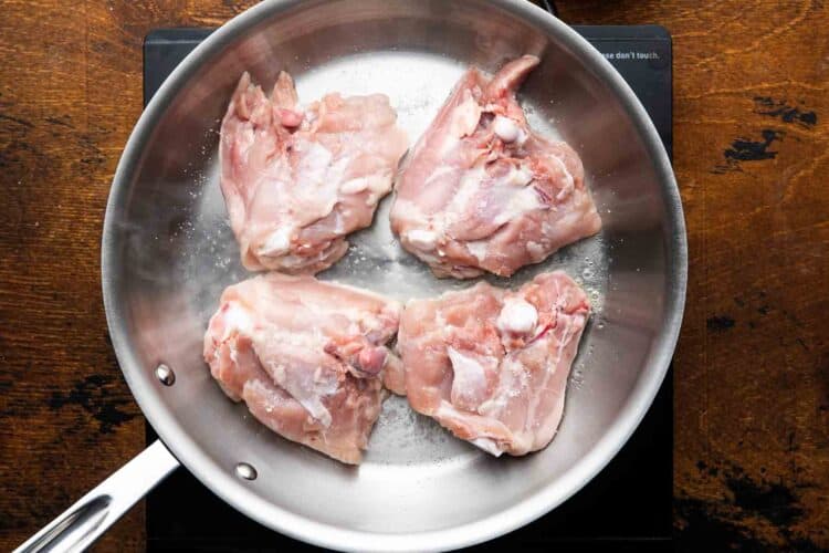 chicken thighs added to a cold stainless steel skillet, skin side down to render the skin.