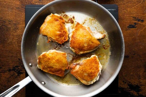 four bone in skin on chicken thighs in a stainless steel skillet with crispy skin.