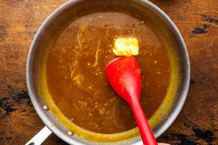 orange sauce cooking in a cast iron skillet, a pat of butter is stirred in to make it glossy and rich.