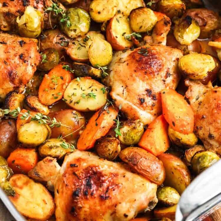 Chicken thighs and roasted vegetables in a metal roasting pan, garnished with fresh thyme.