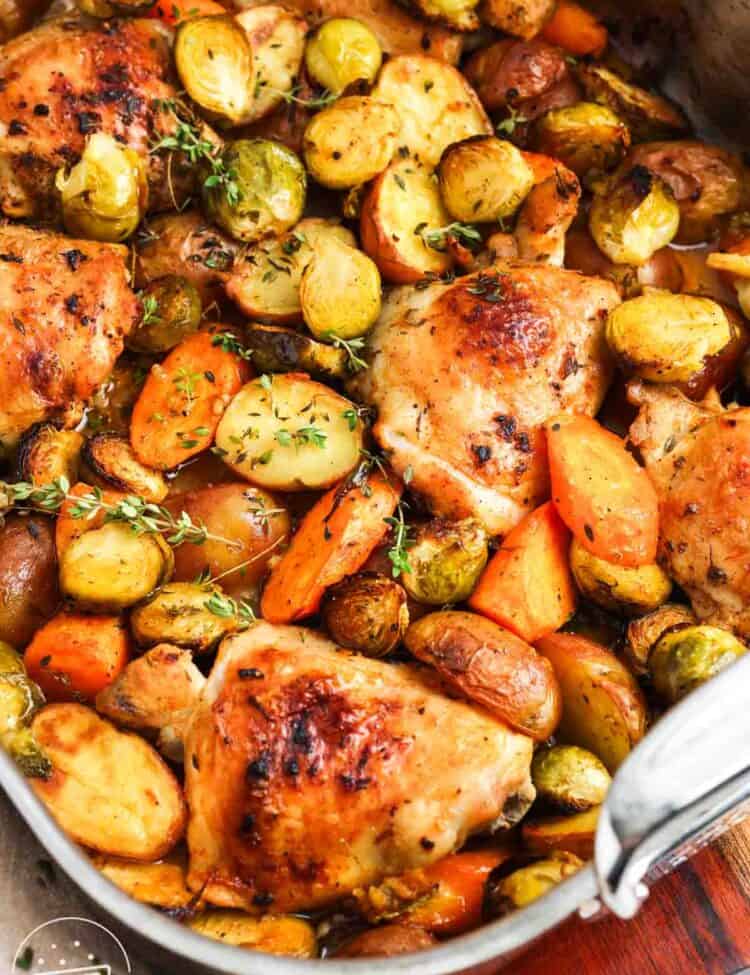 Chicken thighs and roasted vegetables in a metal roasting pan, garnished with fresh thyme.