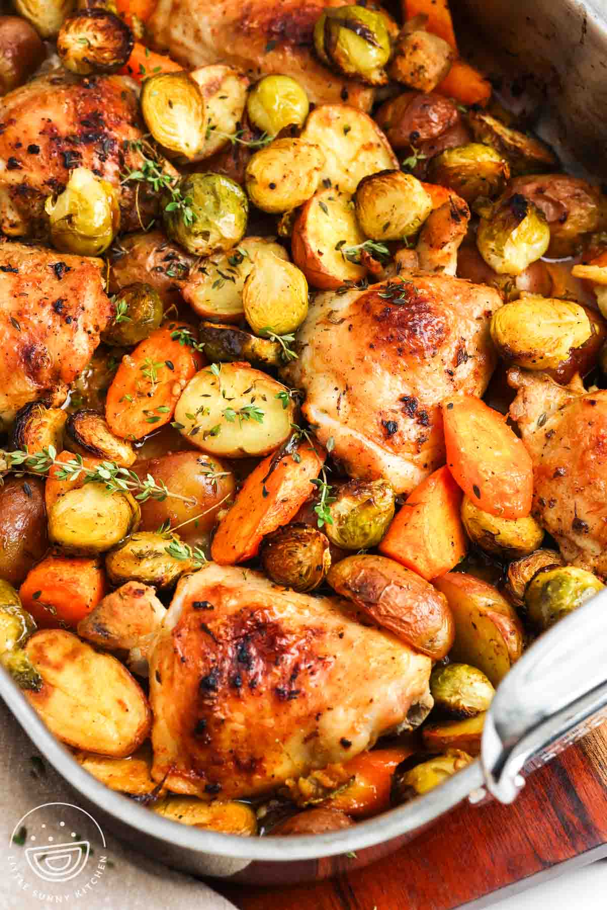 Chicken thighs and roasted vegetables in a metal roasting pan, garnished with fresh thyme.