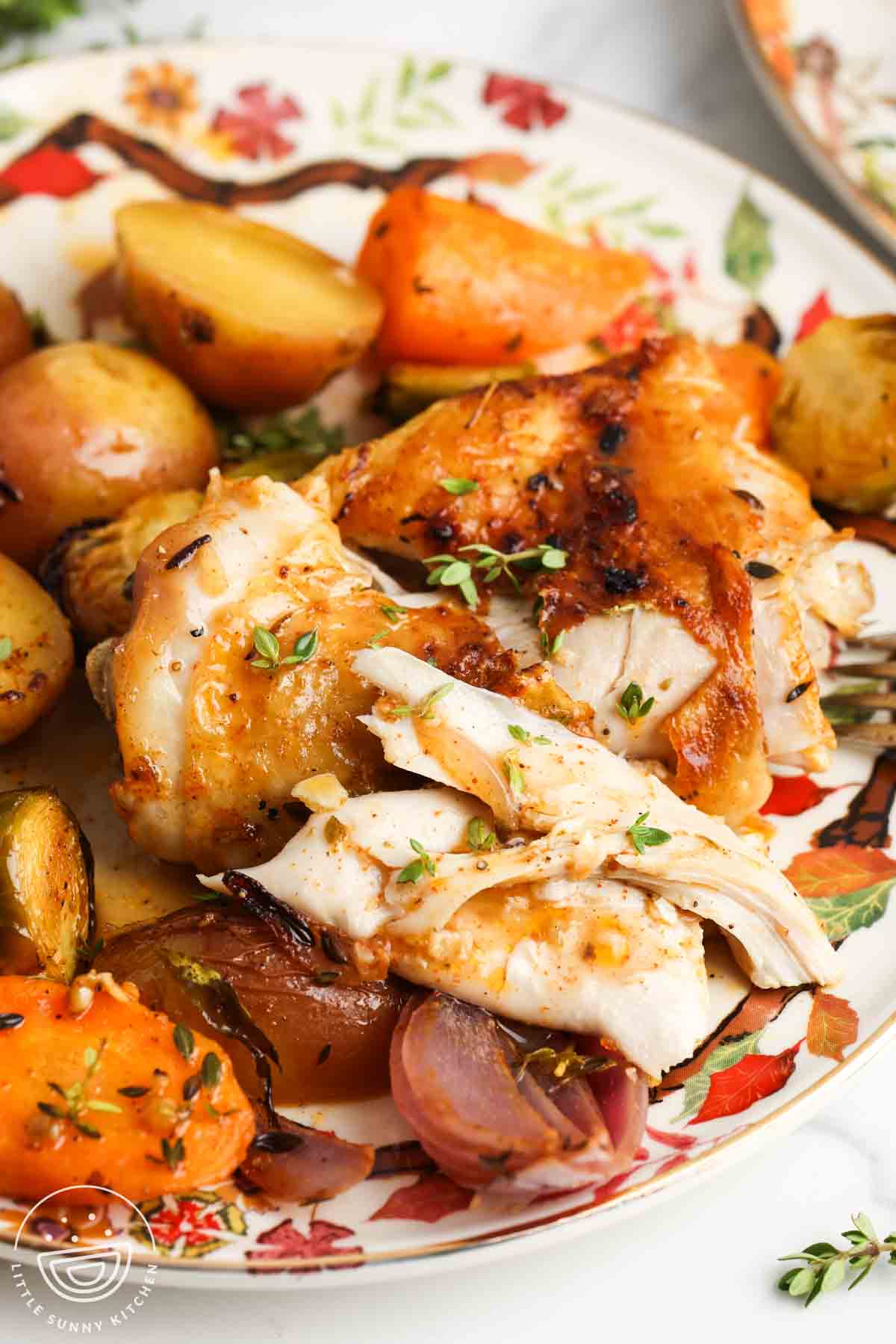 Tender chicken thigh, cut in half, on a plate with roasted vegetables.