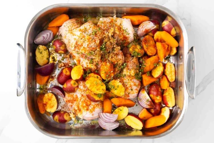 raw chicken thighs in a roasting pan with potatoes, and onions, sprinkled with olive oil and seasonings.