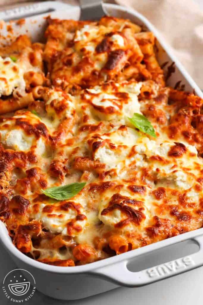 a white ceramic pan of baked ziti with browned cheese on top.