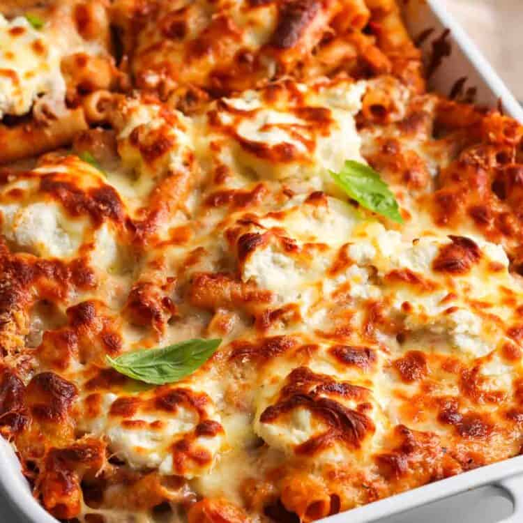 a white ceramic pan of baked ziti with browned cheese on top.