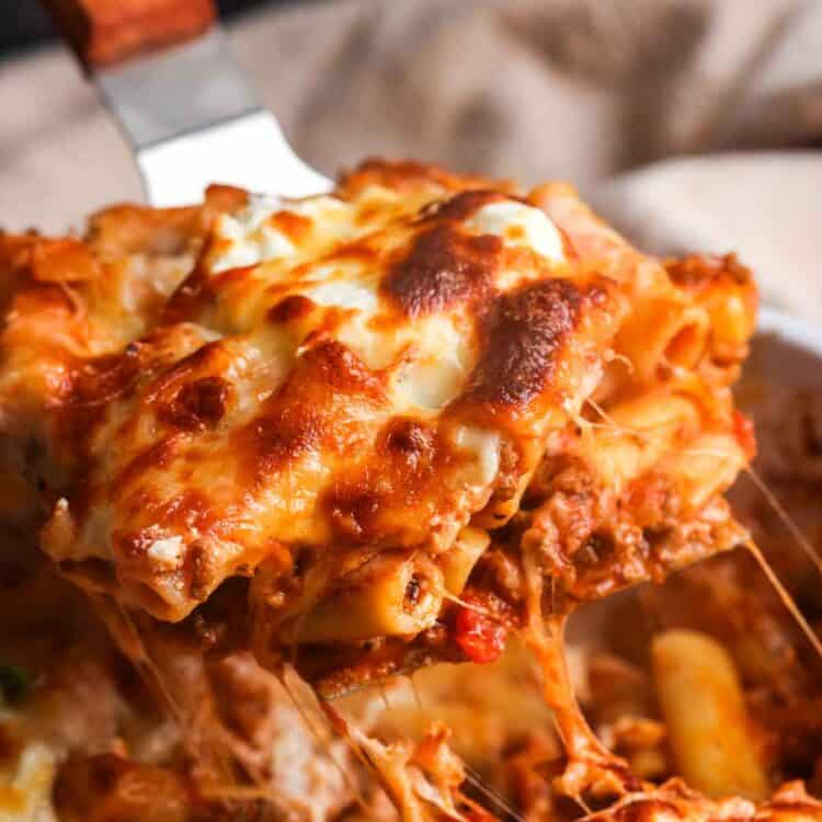 a square of baked ziti lifted out of the pan with a spatula to show the meaty, saucy pasta and lots of melted cheese.