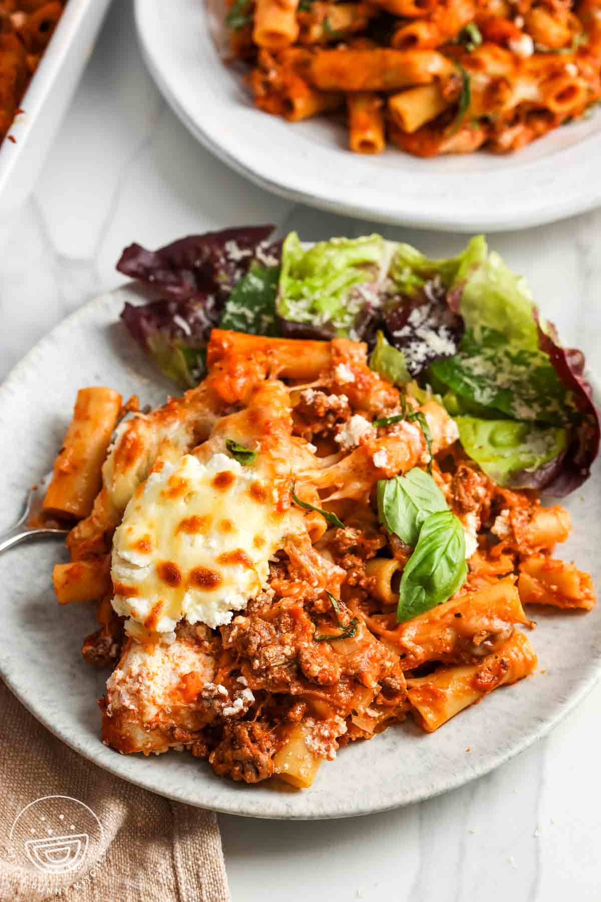 a dinner plate of baked ziti with ricotta cheese with a side of salad.