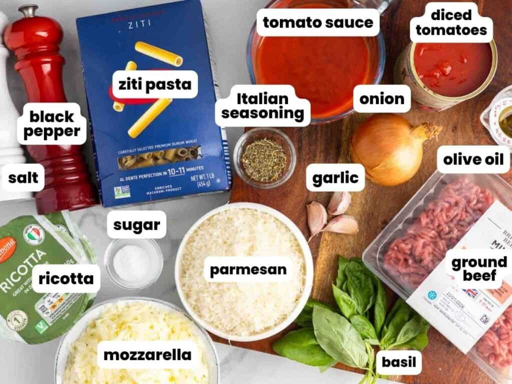 Ingredients for easy baked ziti with ground beef and ricotta, arranged on a counter with a wooden cutting board.