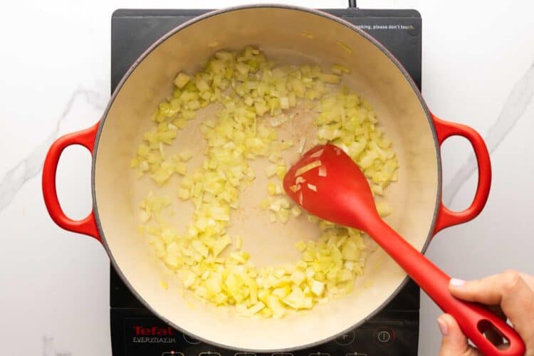diced onions sauteed in a dutch oven, stirred with a red spoon.