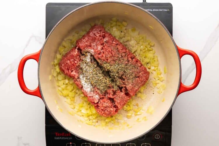 ground beef and seasonings added to a dutch oven with sauteed diced onions.