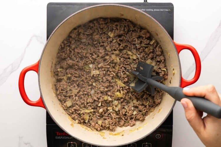 ground beef cooking in a dutch oven, broken up with a meat chopper tool.