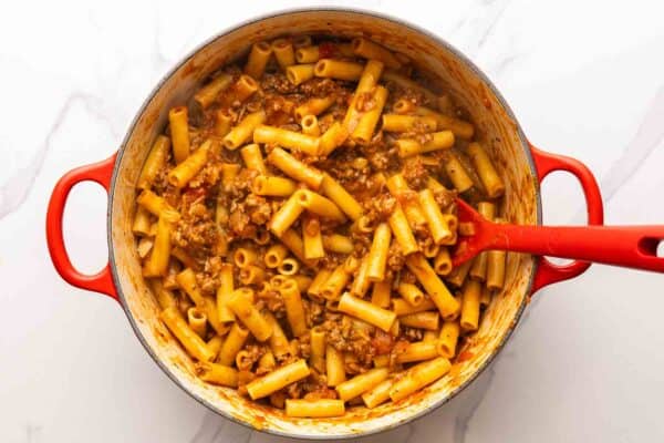 cooked ziti is stirred into a homemade meat sauce in a pot.