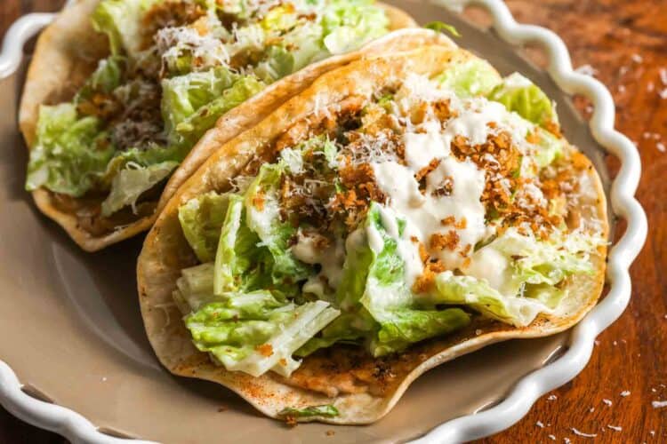 Caesar chicken smash tacos with ground chicken cooked on flour tortillas topped with chopped romaine lettuce Caesar dressing grated Parmesan and toasted panko on a plate.