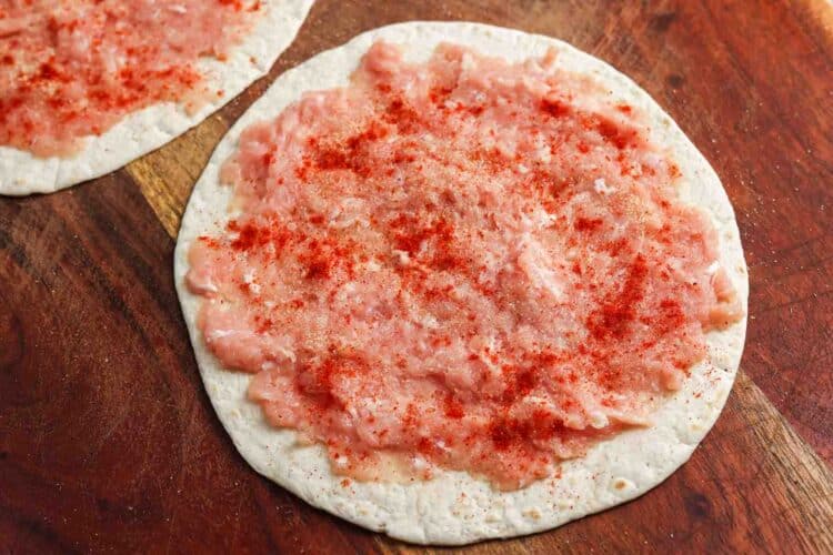 Ground chicken pressed into a thin layer on flour tortillas and seasoned with smoked paprika, garlic powder, salt, and black pepper on a wooden board.