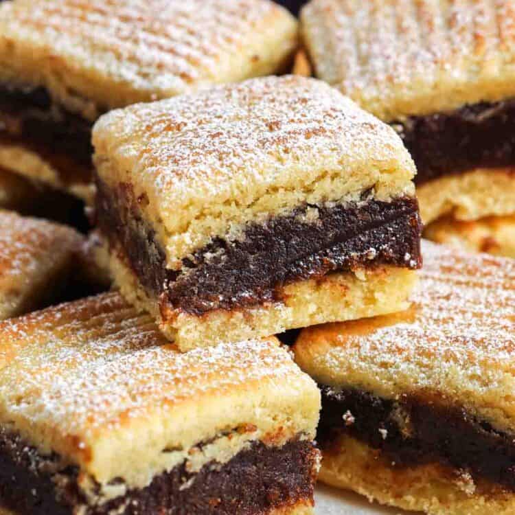 Close-up of stacked semolina date bars showing the thick date filling between golden layers, lightly dusted with powdered sugar.