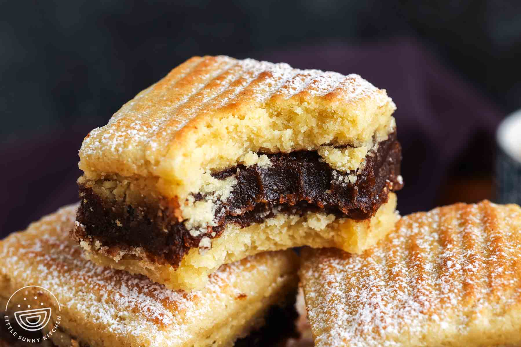 Single maamoul semolina date bar resting on other bars, showing the soft crumb and dense date filling inside.