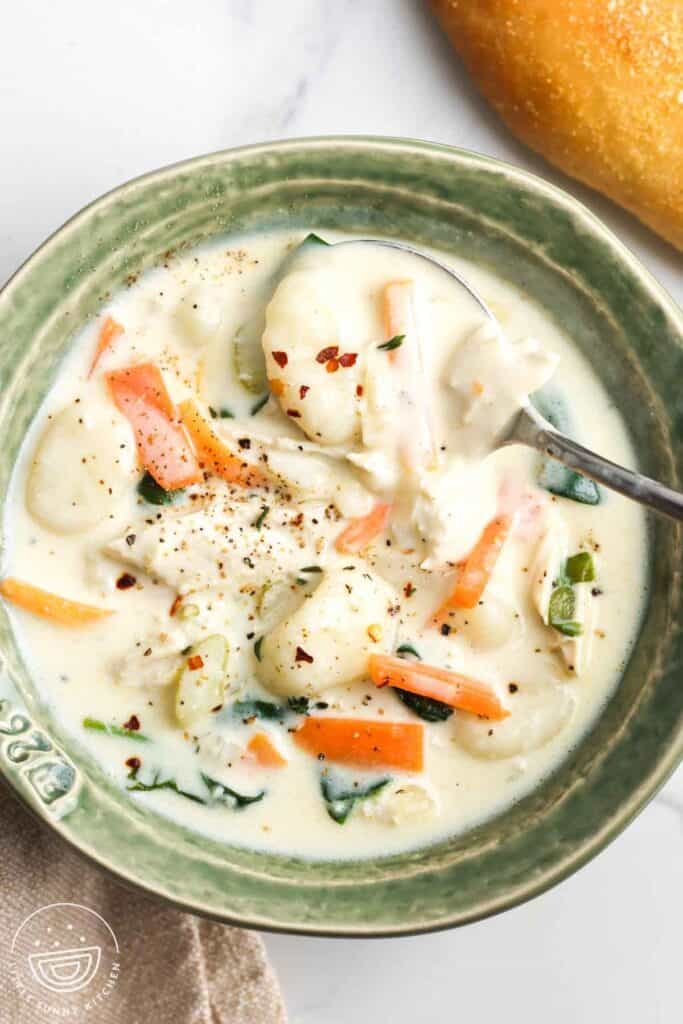 a rustic green ceramic bowl of homemade chicken and gnocchi soup seasoned with crushed red pepper.