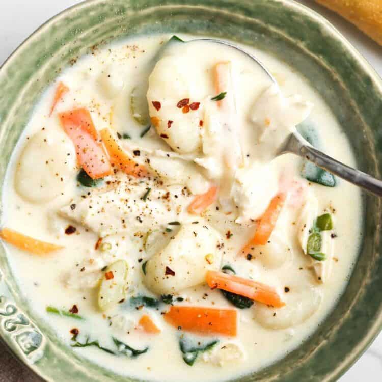 a rustic green ceramic bowl of homemade chicken and gnocchi soup seasoned with crushed red pepper.