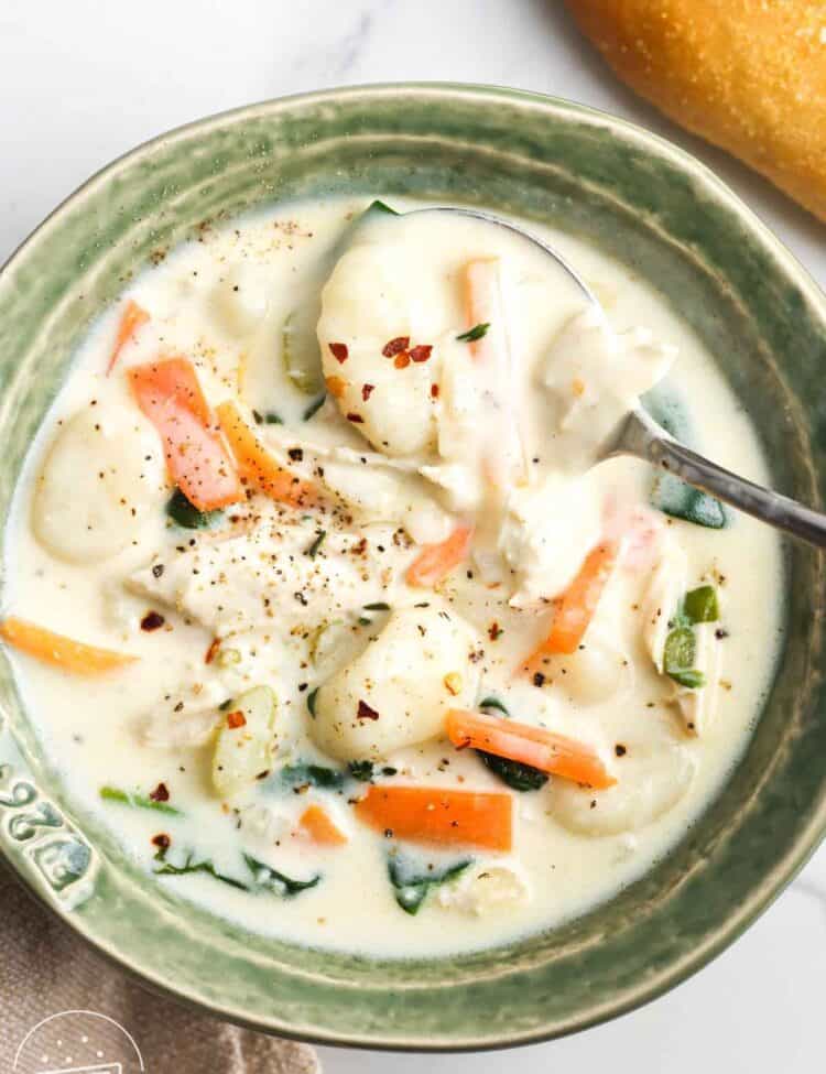 a rustic green ceramic bowl of homemade chicken and gnocchi soup seasoned with crushed red pepper.