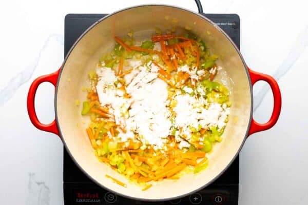 Flour added to sauteed soup veggies in a red enameled dutch oven.