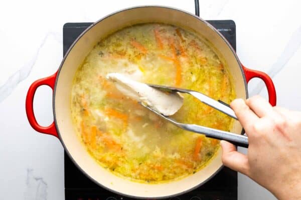 tongs used to removed cooked chicken breast from a pot of soup.