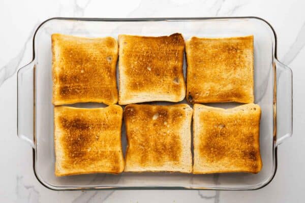 Toasted slices of bread arranged in a 9x13 glass baking dish