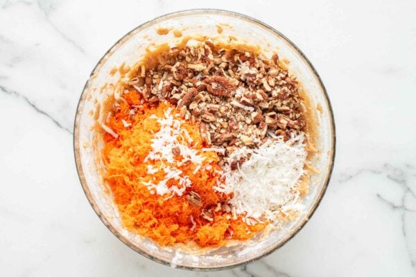 chopped pecans, shredded coconut, and grated carrots added to cake batter in a large mixing bowl.