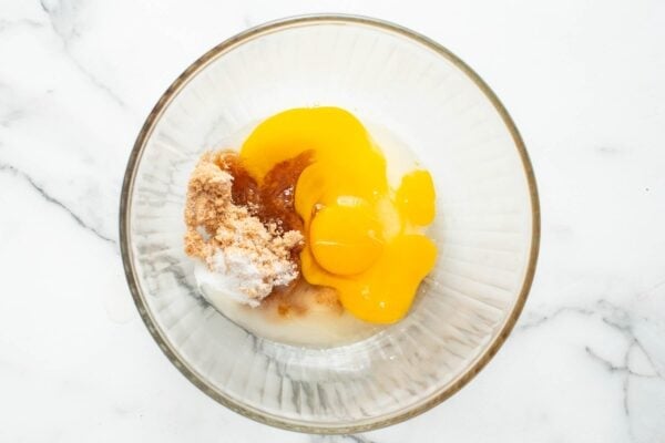 Eggs, sugar and brown sugar in a glass mixing bowl set on a marble counter.
